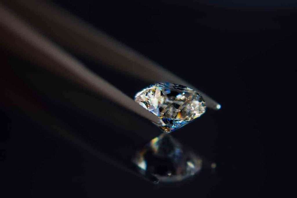 Diamond being held by tweezers on a dark background