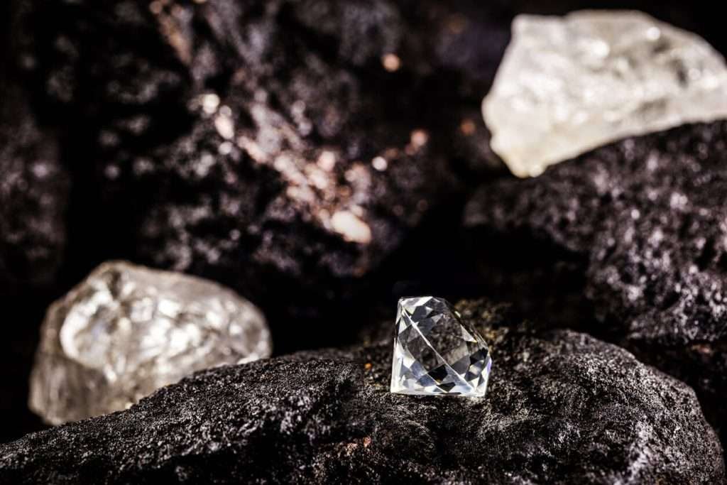 A cut diamond sitting beside raw diamonds