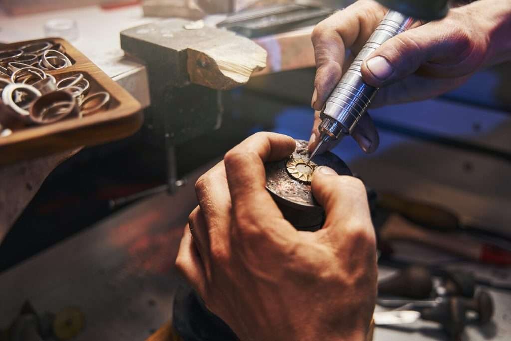 Jeweler's hands carefully engraving a piece of jewelry on a table.