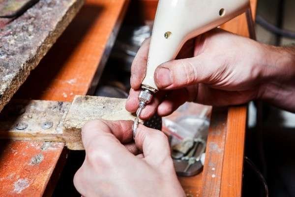 Close-up of a jeweler's hands carefully working on a piece of jewelry with a small machine engraving tool.