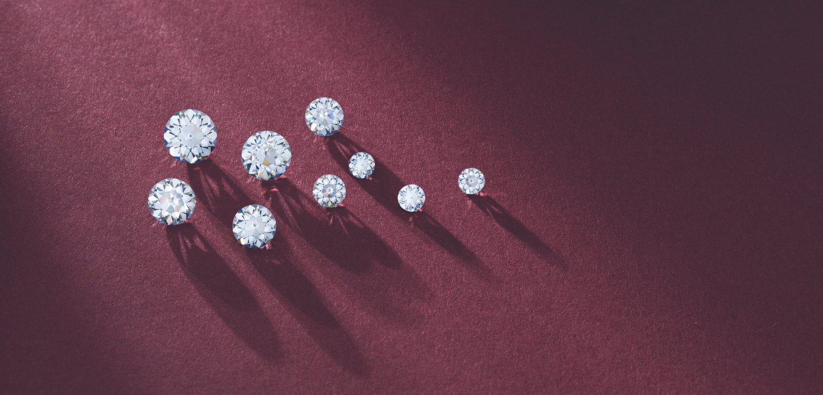 Loose diamonds on a deep burgundy surface with dramatic shadows highlighting their brilliance and varying sizes